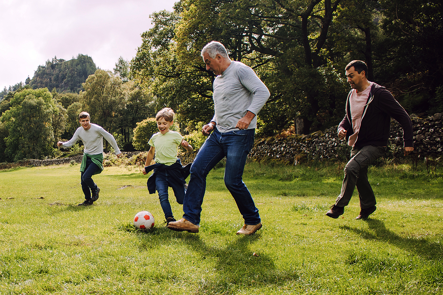 Senior man playing soccer with a young boy and two young adult men. 